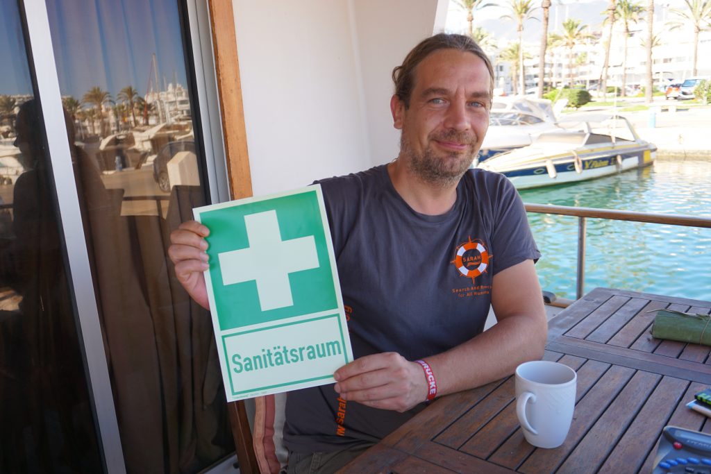 Seenotretter Markus Groda hält ein Sanitätsraum-Schild in die Höhe.